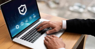 Homem de negócios usando laptop, com uma tela de proteção que representa o sistema antifraude para e-commerce.