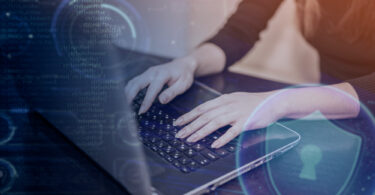 Imagem de uma técnica de TI usando notebook, com símbolos digitais representando a cibersegurança para empresas.